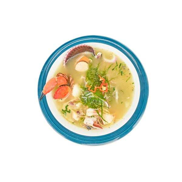 Seafood soup with crab claw, scallops, and green herbs in a blue-rimmed bowl.